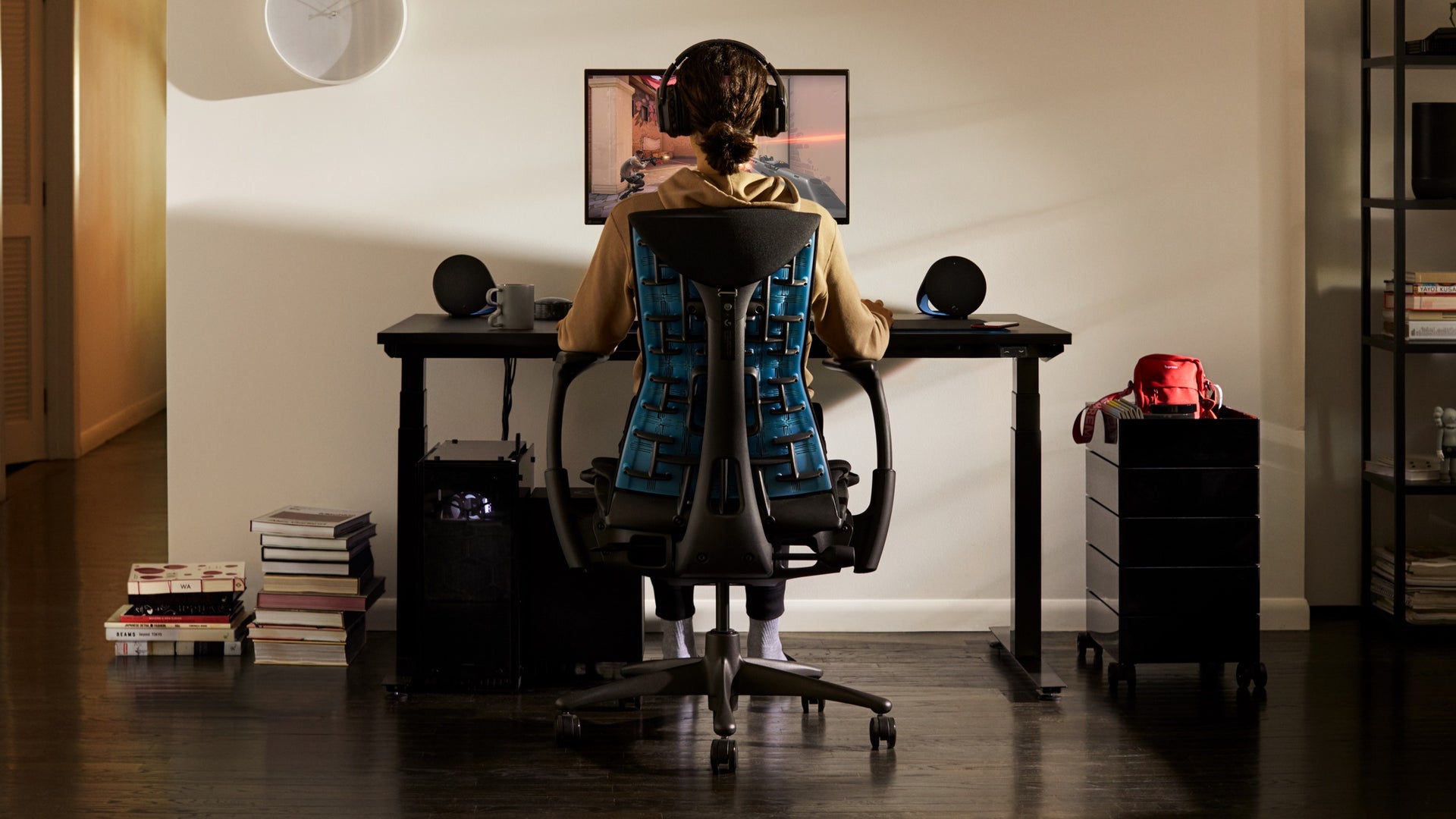 Una persona se sienta en la silla para videojuegos Embody y mira un monitor unido al brazo articulado para monitor Ollin, que se apoya sobre la mesa para videojuegos en un entorno residencial.